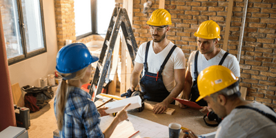 Fire mennesker med hjelmer står på en byggeplass. Foto